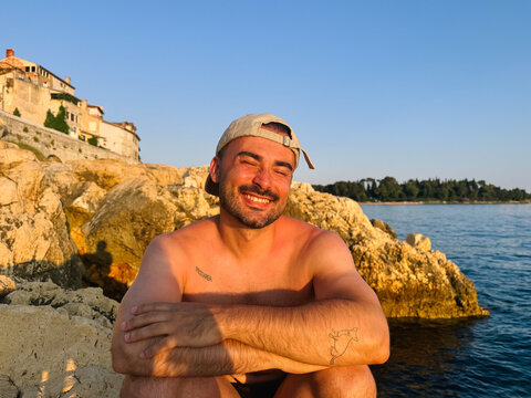 Shirtless Man Crouching on Coastal Rocks During Golden Hour