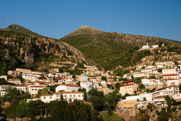Obraz premium Mediterranean hillside town with red roofs and green mountains, real lifestyle travel illustration in warm daylight in Albania