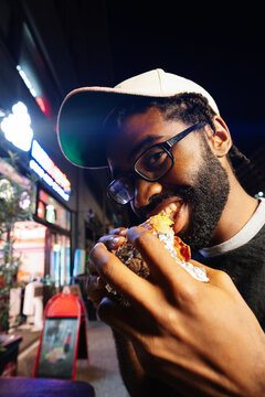 Man Biting Into Street Food At Night