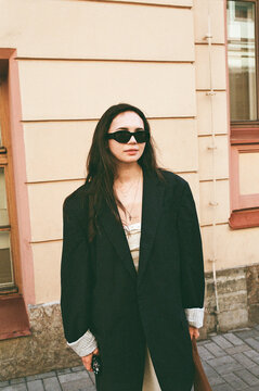 Woman in Black Coat Stands Outside Building With Pink Accents