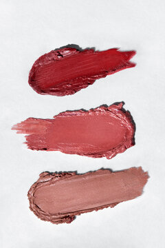 Various swatches of textured red lipsticks on white paper background.