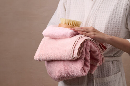 Woman in bathrobe holding stack of soft pink towels and a wooden brush