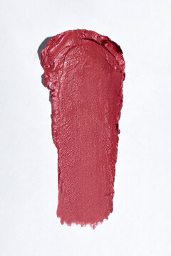 Swatch of bright red lipstick smeared on white paper background.