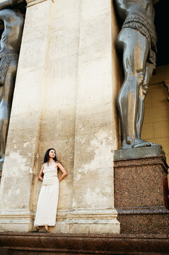 Woman Stands Near Large Stone Statues in a City Setting