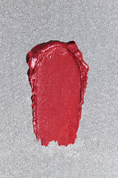 Swatch of bright red lipstick smeared on silver glossy background.