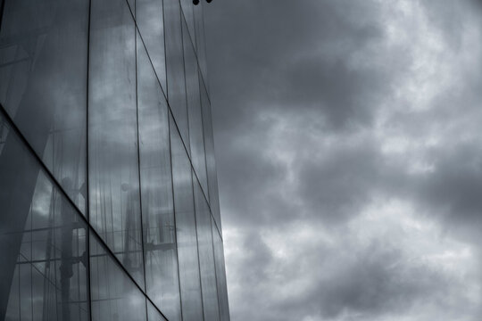 Reflective glass facade mirrors dark storm clouds across vertical panels creating an abstract study of weather and surface across the exterior