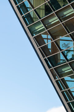 Modern glass architecture with steel framework and transparent panels rises beside blue sky in a minimal geometric exterior detail