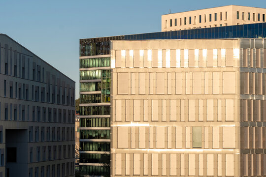 Modern buildings with illuminated windows and warm sunlight create a geometric urban facade where windows repeat across the facade under clear blue sky
