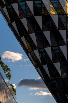 Modern glass facade with angular panels and reflections against the sky creates an abstract study of geometry across the exterior design