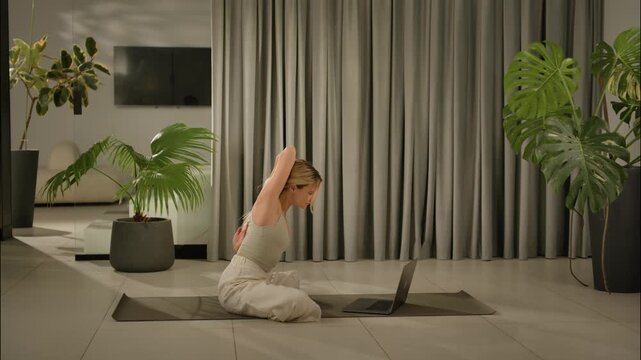 woman practicing yoga in calm indoor space with curtains and houseplants. side view of woman in awh.