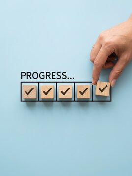 Business Progress Concept with Hand Placing Final Checkmark Wooden Block in Progress Bar on Blue Background