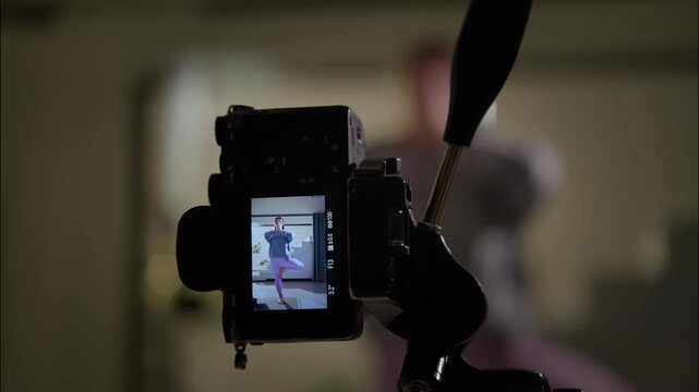 Behind scenes camera setup filming indoor yoga balance pose on tripod with blurred performer in home