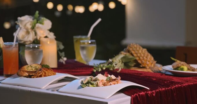 Romantic dinner table with gourmet food and cocktails at night. Elegant dining setting with candles, flowers, and tropical drinks for a couple on a date. Luxury restaurant atmosphere outdoors.