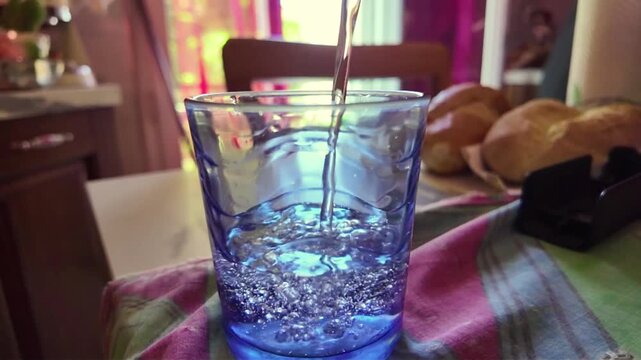 high angle shot of crystal clear water flowing and pouring smoothly into a clear glass in slow motion, water splashing and creating tiny bubbles