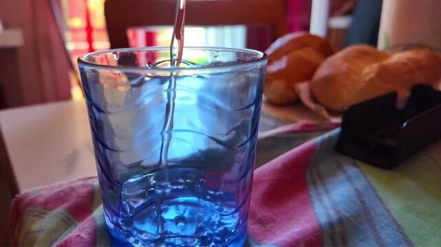 high angle shot of crystal clear water flowing and pouring smoothly into a clear glass in slow motion, water splashing and creating tiny bubbles