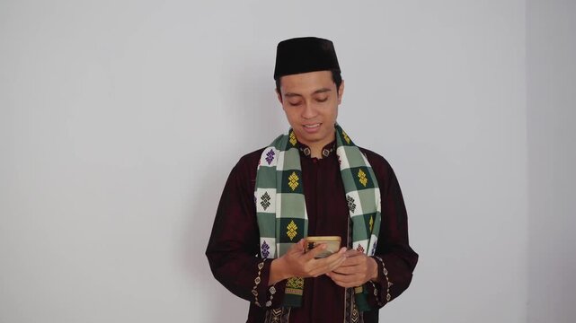 Cheerful Young Man in Traditional Attire Engaging with Phone's Camera on a Light Background