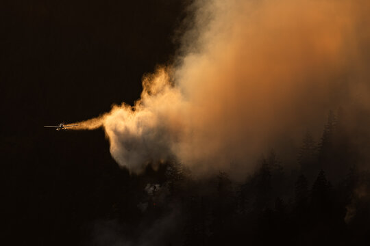 Airplane drops water on a wildfire from above.