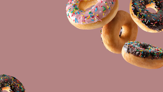 Assorted glazed donuts with sprinkles falling against a solid pink background