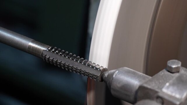 Close up of precision metal threading process on industrial grinding machine in workshop. Rotating steel rod and abrasive wheel during manufacturing operation show machining technology and engineering