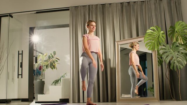 Woman holding tree pose yoga balance in home with mirror, curtains, tropical plants, warm glow light