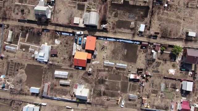 Aerial view shows rural settlement with scattered homes. Fields and unpaved roads divide the structures. Roof colors contrast against earthy surroundings. in this drone shot. Ideal for agricultural