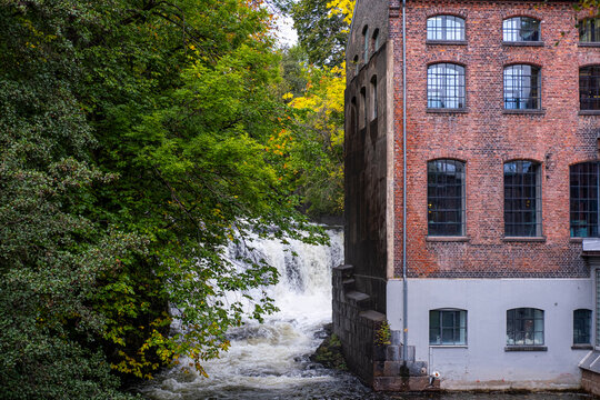 Historic brick building beside a rushing waterfall in Gr&uuml;nerl&oslash;kka Oslo Norway is surrounded by autumn trees and dense urban greenery