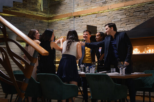 A diverse group of friends enjoy an evening party at a restaurant, sharing joyful moments and toasting their time together.