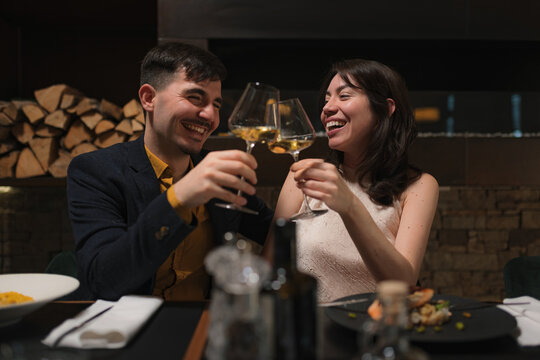 A happy couple celebrates a special occasion by toasting with wine glasses at a restaurant.
