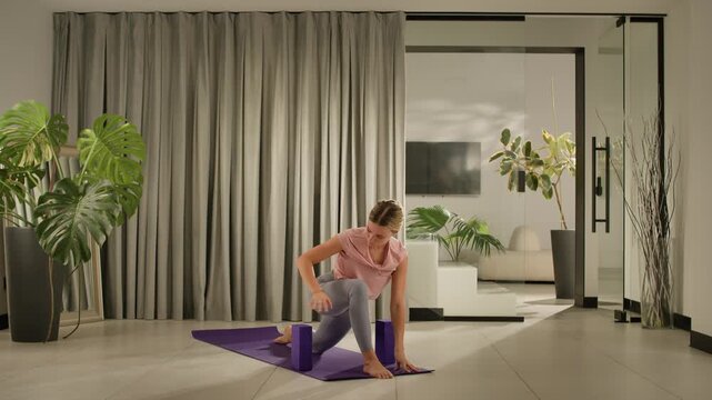 Young woman lifting chest into cobra pose on purple mat inside bright modern living room with plants