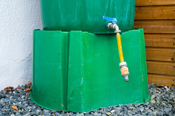 Green plastic water container for rainwater collection stands on gravel near home wall in the garden © Razbitnov