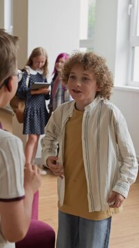 Vertical shot of Caucasian schoolboys greeting with hug and talking in school corridor. Video suitable for back to school campaigns and elementary education marketing