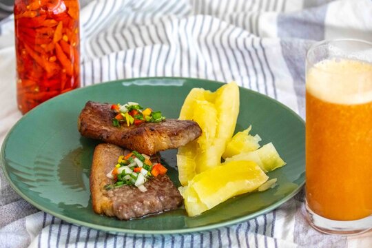 Carne de sol, a traditional northeastern Brazilian dish of salted sun-dried beef served with boiled cassava, fresh onion and bell pepper vinaigrette, chili pepper sauce and acerola juice.