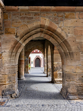 A view through a historic stone archway of a building with window boxes and cobblestones; the arches of the historic town hall in Alsfeld