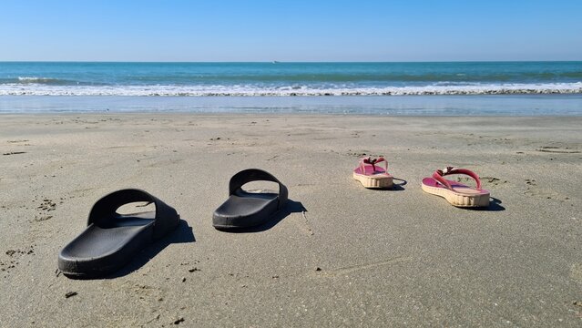 Footwear left on a sandy beach with the ocean waves gently rolling in, capturing a serene moment of relaxation and summer leisure