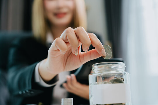 Happy woman performs business tax financial management by putting coin into glass jar with joyful expression for future growth savings
