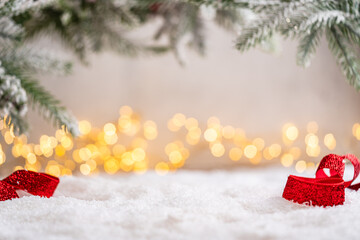 Naklejka premium A Christmas background featuring a sparkling red ribbon on snow beneath frosted pine branches, with wide empty copy space softly lit by warm twinkling lights in the distance.