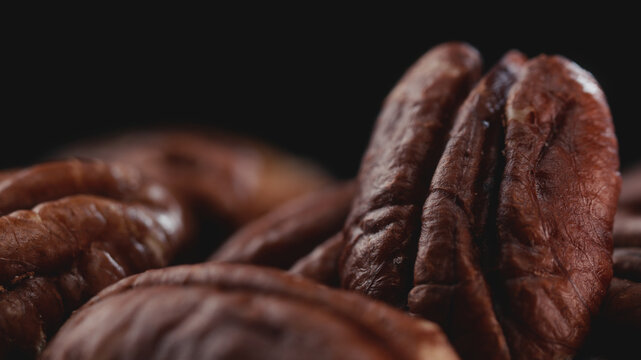 Extreme macro shot of fresh premium pecan nuts with selective focus on dark background with artistic lighting. Perfect for healthy eating, gourmet food, culinary, and dietary content.