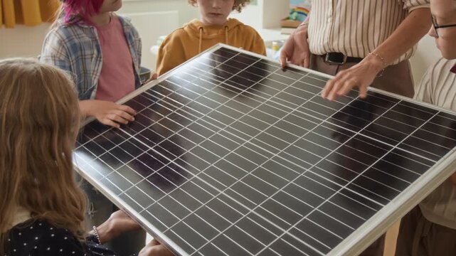 Unrecognizable teacher explaining solar panel to elementary children during STEM science lesson. Clip fits clean energy education, school sustainability curricula and green technology marketing