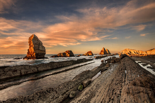 Golden sunset over the flysch formations and rocky islets of Costa Quebrada at Arnia beach in Cantabria, Spain, during low tide
