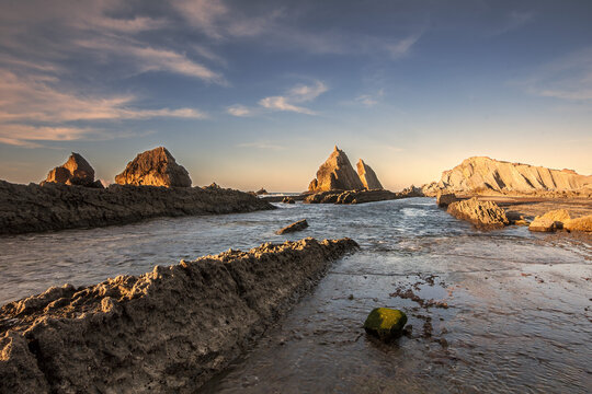 Golden sunset over the flysch formations and rocky islets of Costa Quebrada at Arnia beach in Cantabria, Spain, during low tide