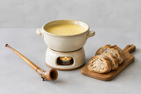 Ceramic cheese fondue pot with melted cheese, bread and carved alphorn, cozy dining concept