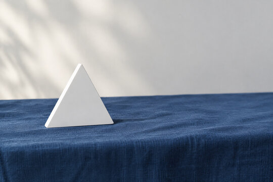 Single white equilateral triangle object on deep blue linen, calm still life for editorial concept