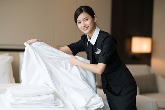 Hotel housekeeper making bed with clean white linens in bright modern guest room interior