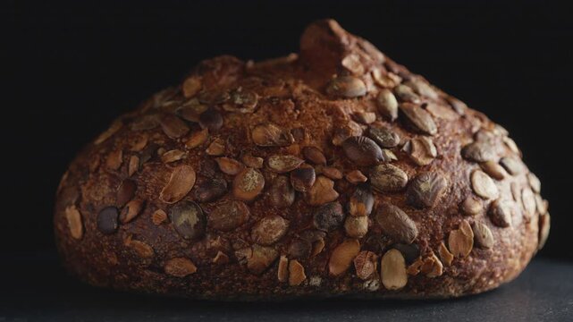 Close-up of artisan whole wheat sourdough bread topped with pumpkin seeds on a dark background. Freshly baked organic loaf with crispy crust for commercial bakery promotions and healthy food concept.