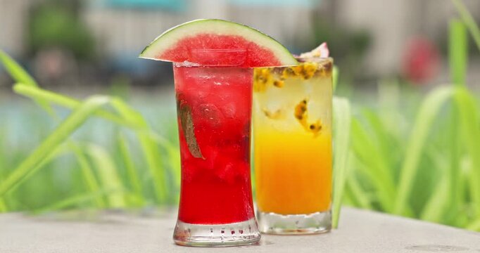 Watermelon and passion fruit cocktails standing on table outdoors. Tropical resort background with green plants and pool. Summer vacation refreshment, luxury travel lifestyle.
