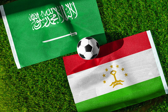 Saudi Arabia vs. Tajikistan football match. National flags on green grass with soccer ball in the middle. Football background for international match.