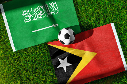 Saudi Arabia vs. Timor Leste football match. National flags on green grass with soccer ball in the middle. Football background for international match.