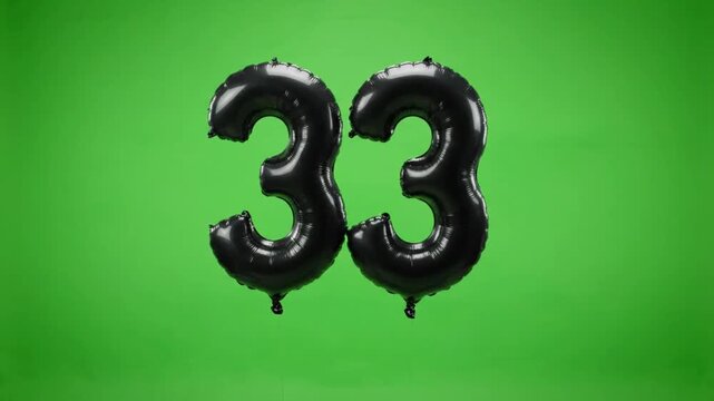 Black foil number Thirty-Three balloon floating up on green screen background