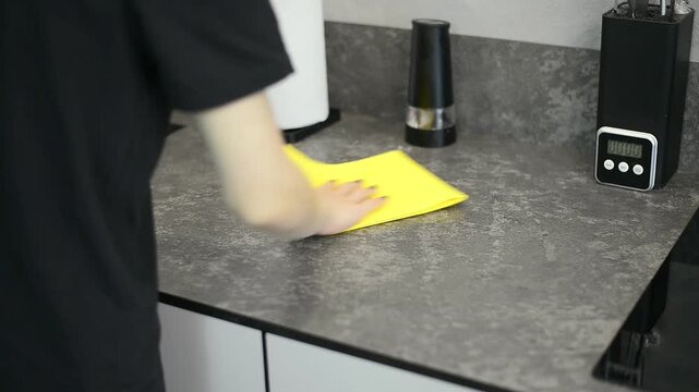 Woman hand wiping a kitchen counter table surface with a yellow cloth