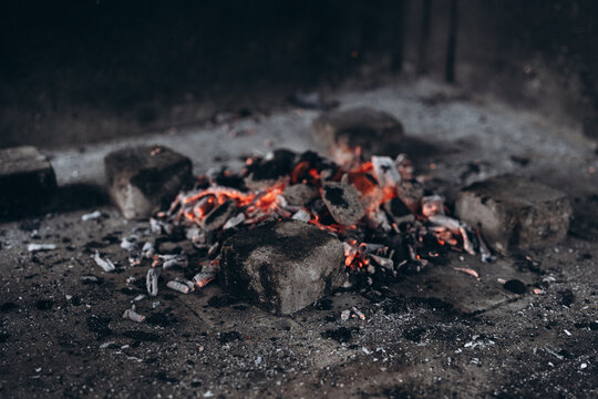 Campfire embers with small flames among black charcoal and ash